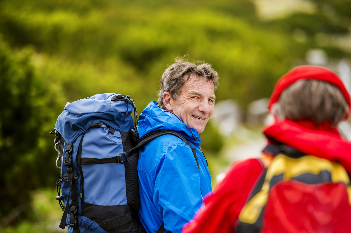 A man in a blue hiking jacket smiling back at a woman in a red jacket on the trail