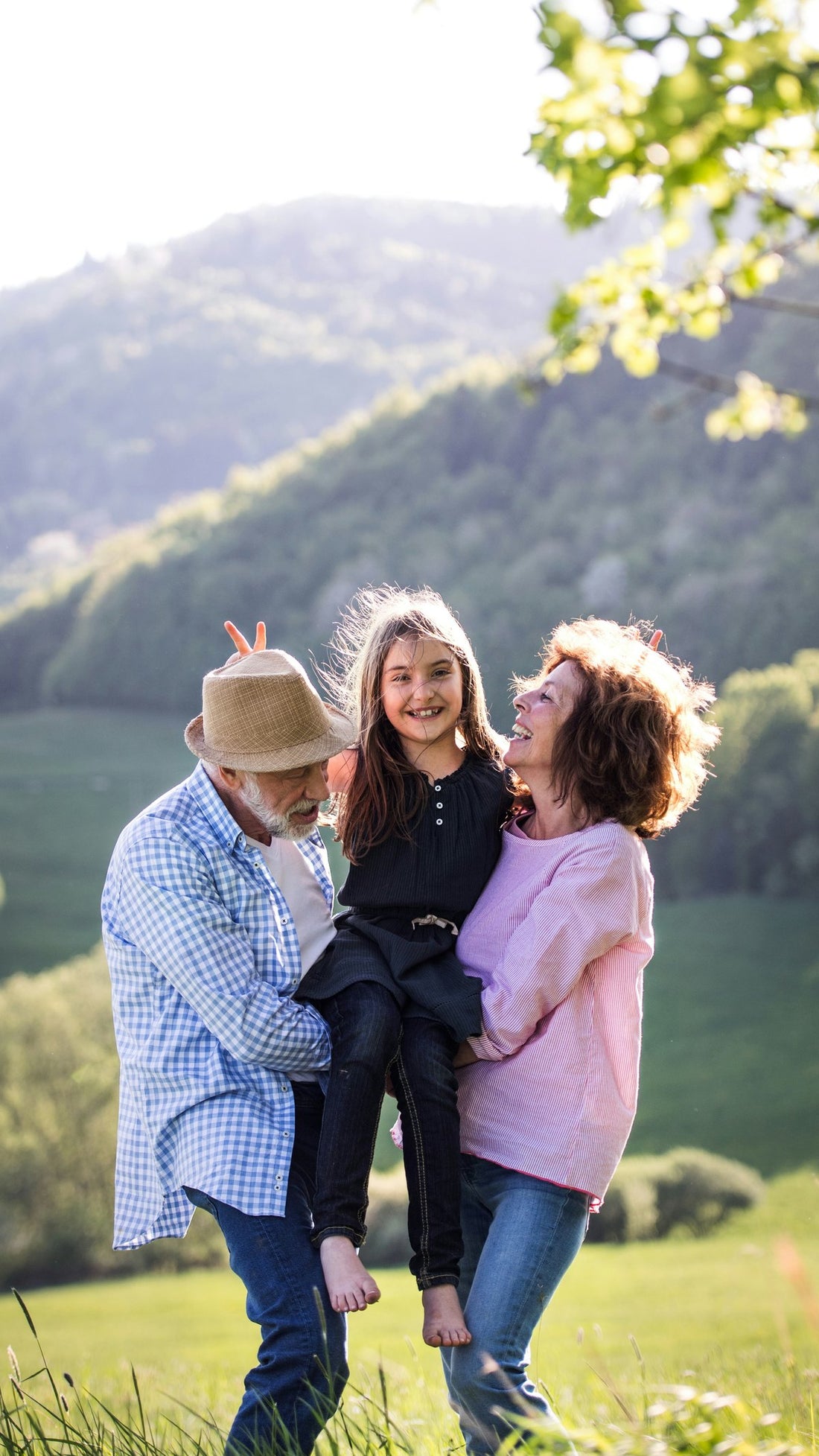 Grandparents holding up their smiling granddaughter in a green valley