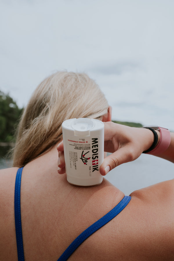 A woman applying the Power Stick to her back by a lake
